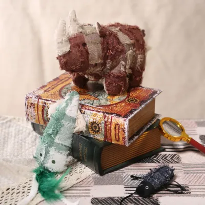 A group of hippie style plush pet toys including a rhinoceros and a green chameleon on vintage books.