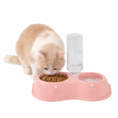An orange and white cat eating kibble from a pink 2-in-1 automatic water dispenser and food bowl set.