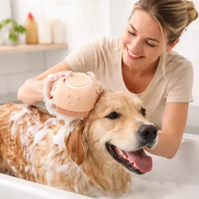 A woman smiling while using an orange silicone brush to bathe a Golden Retriever in a tub.