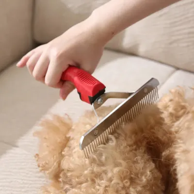 professional-pet-grooming-rake-in-action A close-up of a red-handled pet grooming rake being used to brush through the thick, curly fur of a light brown dog.