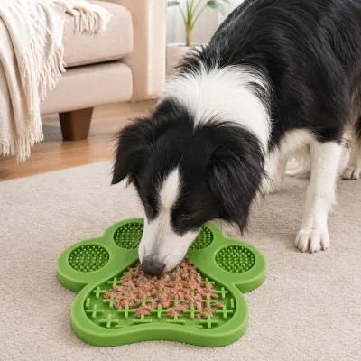 Border Collie Dog Using Green Silicone Lick Mat on Carpet A black and white Border Collie licking wet dog food from a green paw-shaped slow feeder mat on a living room rug.