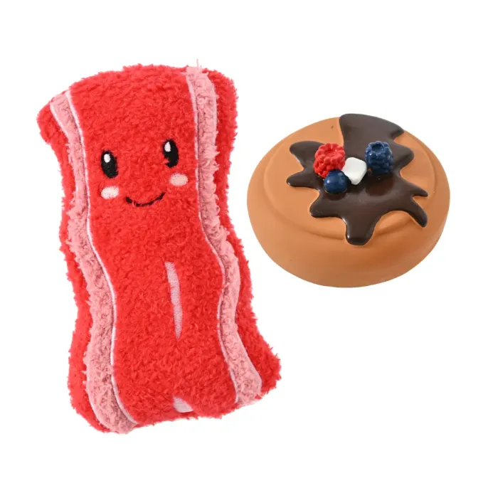 A 2-piece dog toy set featuring a red smiling plush bacon strip and a brown latex donut with berry toppings.
