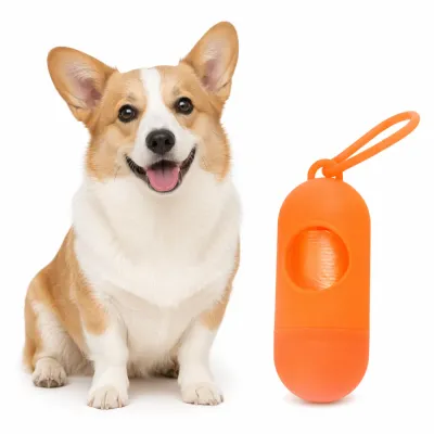 A happy Corgi dog sitting next to an orange pill-shaped pet waste bag dispenser on a white background.