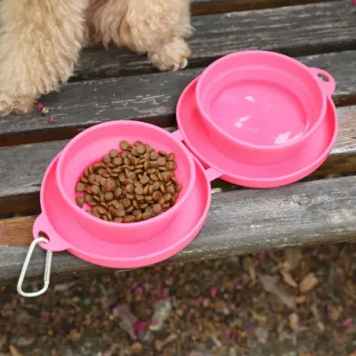 pink-silicone-travel-dog-bowl-food-water Close-up top view of an open pink silicone travel feeder with kibble in one bowl and water in the other on a wooden surface.