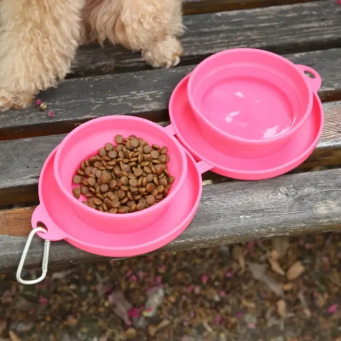 pink-silicone-travel-dog-bowl-food-water Close-up top view of an open pink silicone travel feeder with kibble in one bowl and water in the other on a wooden surface.