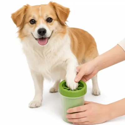 happy-corgi-and-owner-using-green-dog-paw-cleaner A person's hand with a watch guides a fluffy, smiling Corgi-type dog's white paw into a small, green silicone paw washer cup, while another small, brown dog waits nearby. All are set against a plain white background.