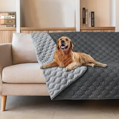 reversible-waterproof-furniture-protector-dog Reversible grey quilted dog blanket draped over a modern sofa with a dog lying down.