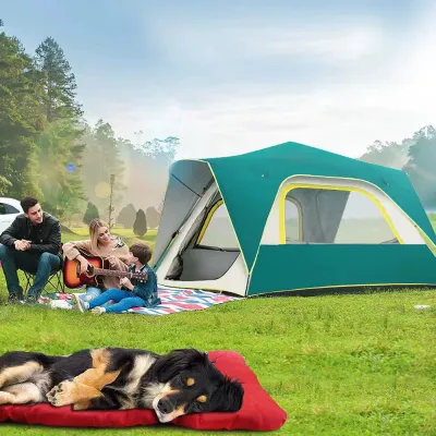 Outdoor-Camping-Dog-Bed-Usage A dog sleeping on a red waterproof mat outdoors while a family sits by a tent in a grassy field.