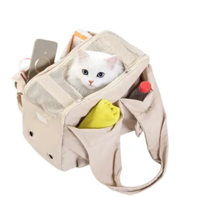 breathable-cat-carrier-tote-functional-pockets A white cat sitting inside a beige pet carrier tote bag showing multiple storage pockets filled with a phone, towel, and water bottle.