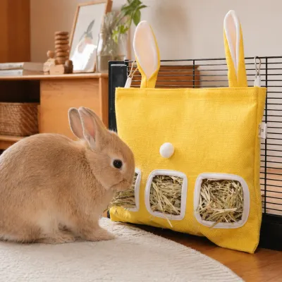 A small brown rabbit eating hay from a yellow hanging feeder bag attached to a black wire cage.