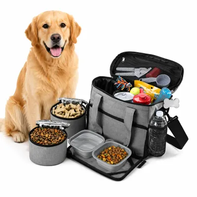 A golden retriever sitting next to an open grey dog travel bag containing toys, food containers, and pet supplies.