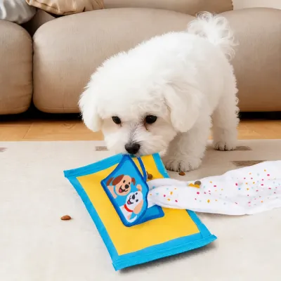 Puppy Playing with Tissue Box Snuffle Dog Toy Small white puppy playing with yellow and blue tissue box dog toy during indoor enrichment and treat hunting game