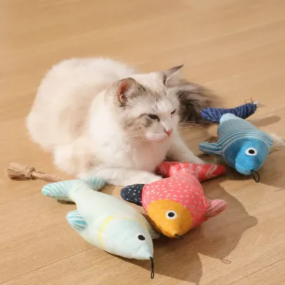 Indoor Cat Playing with Plush Fish Cat Toys | Petfairs Fluffy indoor cat relaxing and playing with colorful plush fish cat toys on wooden floor