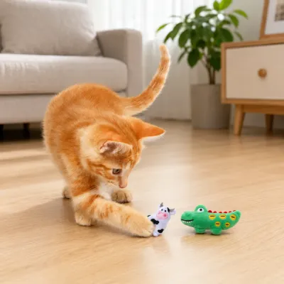 Orange kitten playing with crocodile and cow plush catnip toys on indoor floor