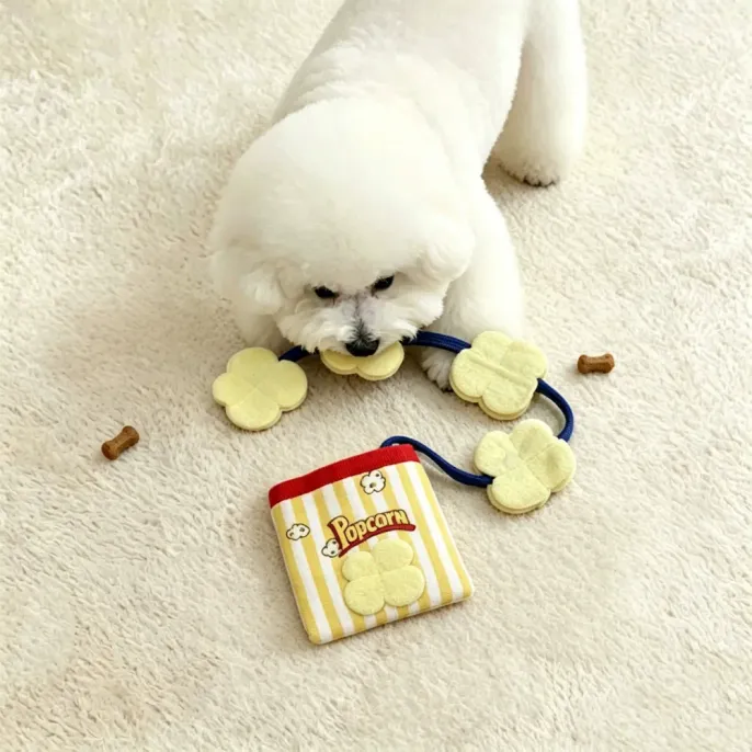 Small white dog playing with plush popcorn crinkle treat pouch toy on soft indoor carpet