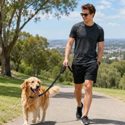 Man walking a golden retriever outdoors using a reflective dog leash with poop bag holder