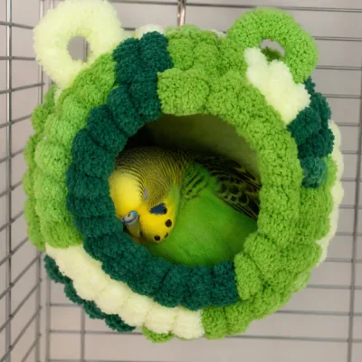 Budgie sleeping inside a warm plush bird nest hut hanging in a bird cage