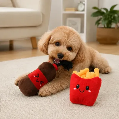 Small dog chewing a soda bottle plush toy beside a red French fries dog toy on a living room rug