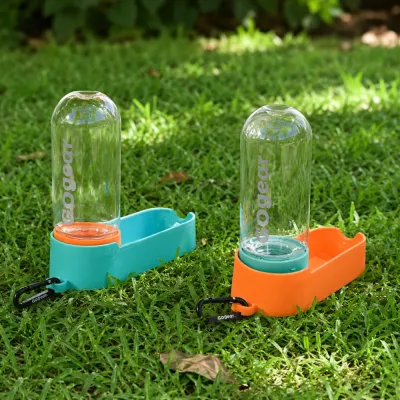Two portable dog water bottles with built-in drinking trays and carabiner clips placed on grass
