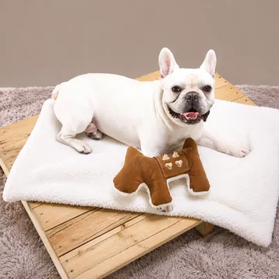 White French bulldog lying on the fluffy sherpa side of a reversible dog mat with matching pet toy