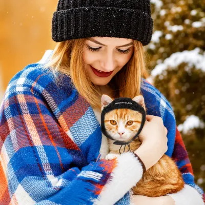 Cat Aviator Hat for Winter Wear and Photos Orange cat wearing a black aviator hat while being held outdoors in a snowy winter setting