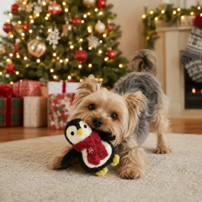 Small dog playing with a Christmas penguin plush dog toy in a festive living room